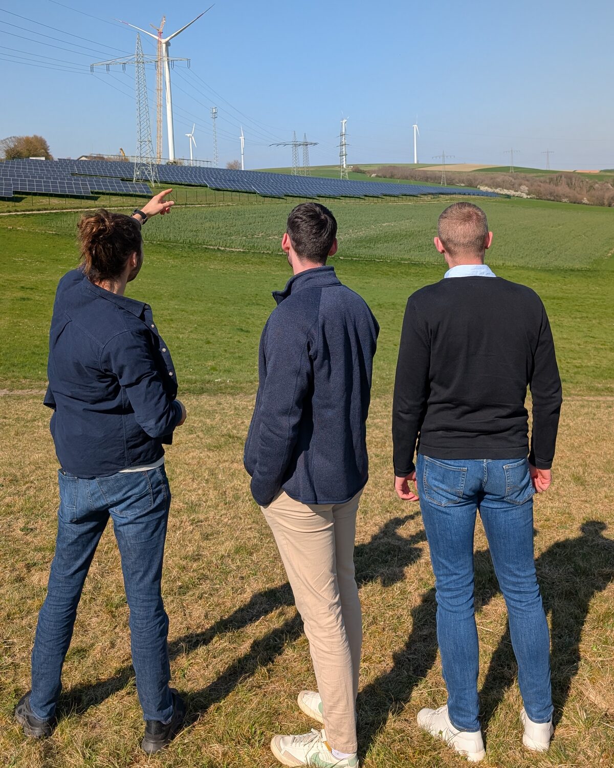 Das Gründerteam von aimpera blickt auf Photovoltaik- und Windkraftanlagen in der Landschaft
